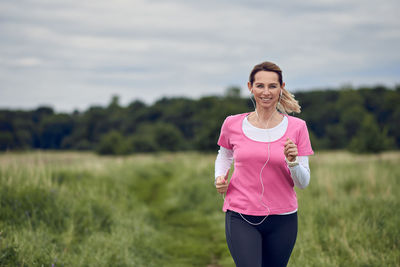 Portrait of smiling woman listening music while jogging against clear sky