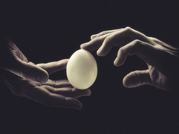 Cropped hands holding egg against black background