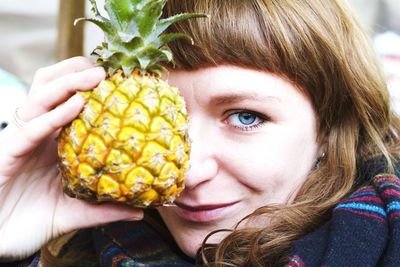 Close-up portrait of smiling young woman showing pineapple