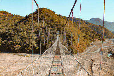 Footbridge amidst trees against sky