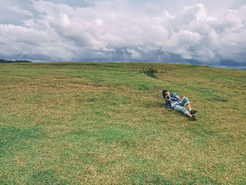 People sitting on field by land against sky