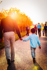 Rear view of father holding hands of son while walking on footpath