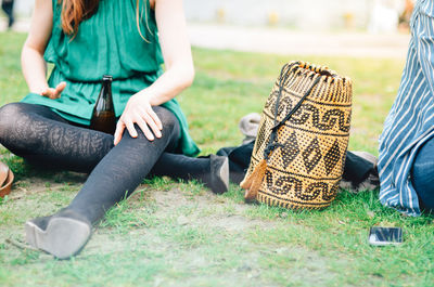 Low section of woman with bottle relaxing by bag on field