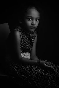 Portrait of cute girl sitting against black background
