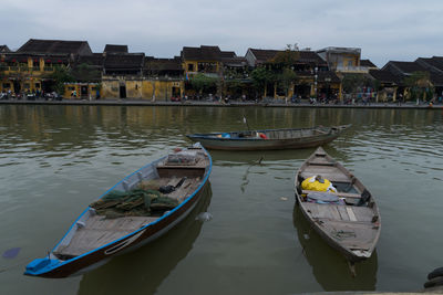 Boats moored in canal by buildings against sky