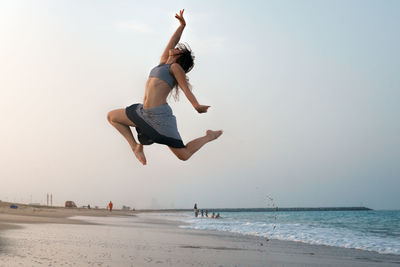 Woman jumping on beach against clear sky