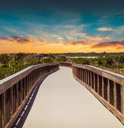 Footbridge over river against sky during sunset