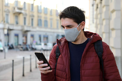 Man wearing mask using phone while standing outdoors