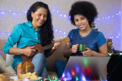 Smiling mother and daughter holding coffee cup while video conferencing over laptop