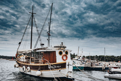 Fishing boats moored at harbor against sky