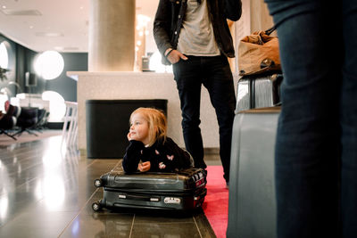 Thoughtful girl with hand on chin leaning on suitcase in hotel