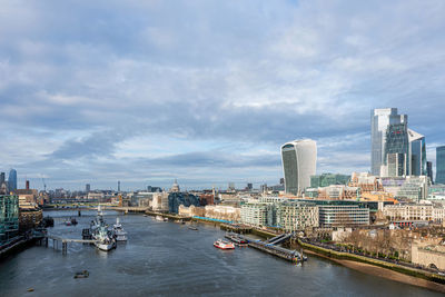 Boats in river by buildings in city against sky