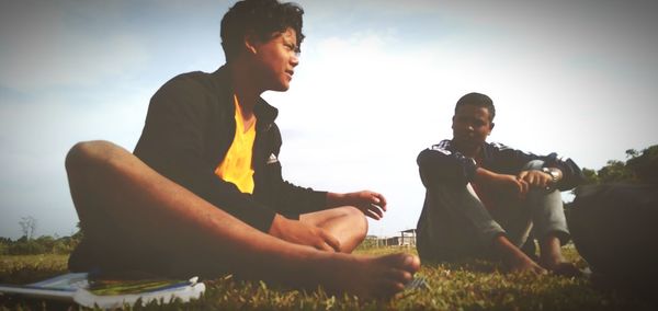 Men sitting on field against sky