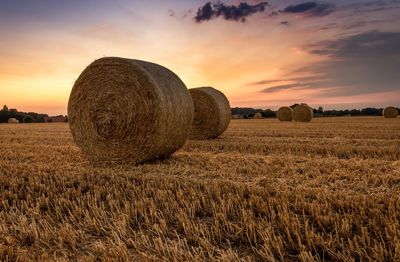 Hay bales on field against sky during sunset