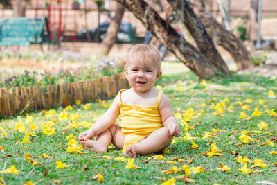 Cute baby girl with blond hair on grass with yellow flowers. summer sunny day in park.