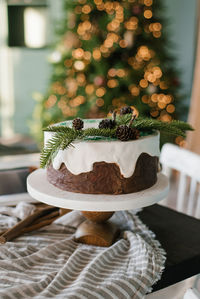 Festive christmas cake with white icing decorated with spruce branches stands on a set table against