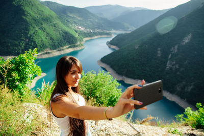 Young woman taking selfie against river