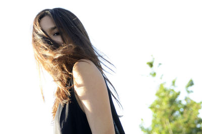 Low angle portrait of teenage girl with tousled hair against sky