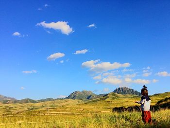 Girl standing on field against blue sky
