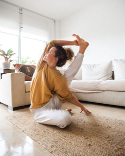 Calm woman in casual clothes sitting on floor and performing surya yantrasana asana while practicing yoga in light living room at home