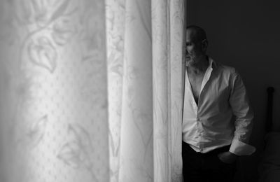 Monochrome of adult man in white shirt in room looking though window