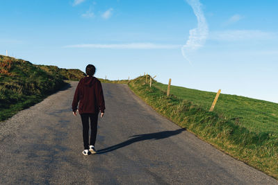Rear view of woman walking on road against blue sky