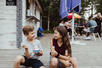 Smiling brother and sister eating sweet food while sitting on wooden floor