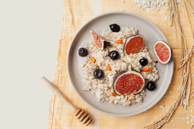 Cereal porridge, blueberries, figs and sea buckthorn on yellow napkin, honey stick and dried flowers