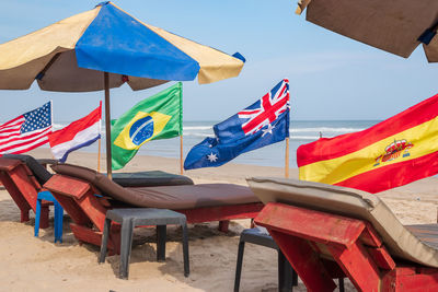 Flags from different countries on the beach with empty sunbeds waiting for new tourists.