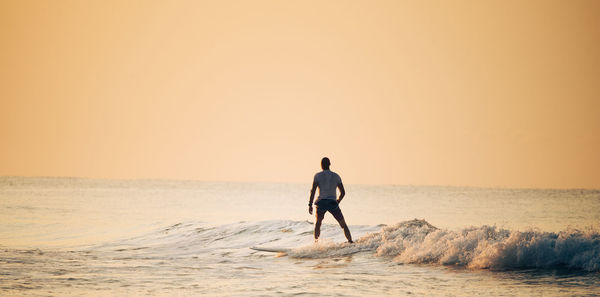 Rear view of man on beach against sky during sunset