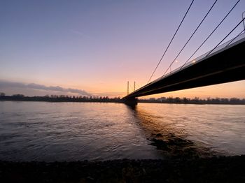 Silhouette bridge over sea against sky during sunset