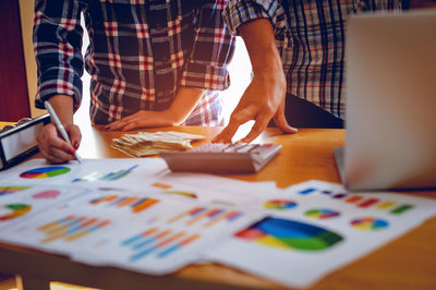 Midsection of colleagues discussing graphs on desk in office