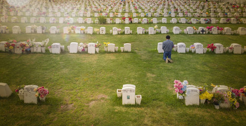 Rear view of man kneeling by tombstone on field during sunny day