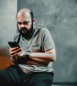 Man holding smart phone while sitting on wall