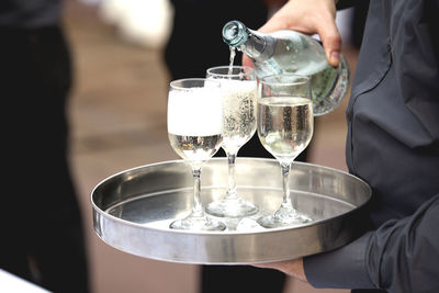 Midsection of waiter pouring wine in glasses