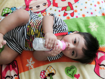 Portrait of cute boy drinking milk from baby bottle while lying on bed at home