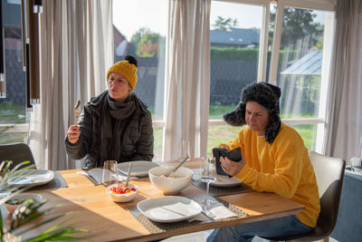 A couple is sitting at the dining table in winter clothes at home, it is cold, they are freezing