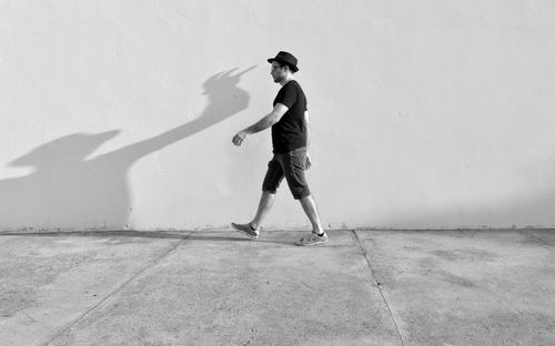 Full length of man walking on sidewalk by wall