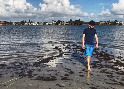 Rear view of boy standing at beach against sky