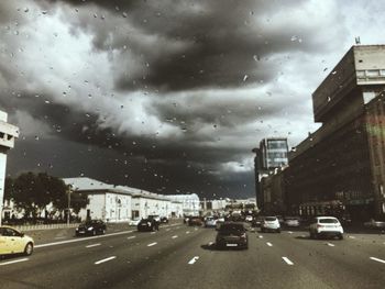 Road passing through city against cloudy sky