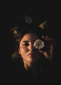 Portrait of woman holding flower against black background