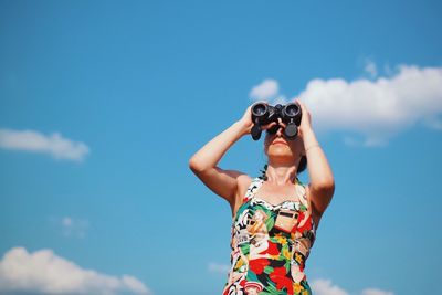 Low angle view of woman looking through binoculars against blue sky