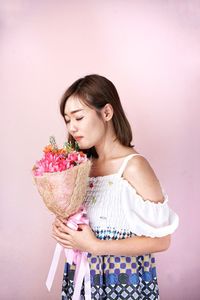 Young woman holding pink while standing against wall