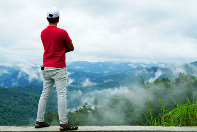 Rear view of man standing on mountain against sky