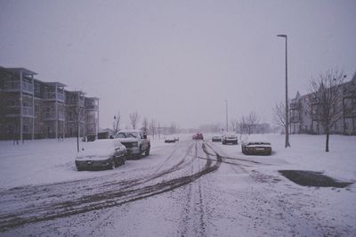 Cars and road covered with snow in city against sky