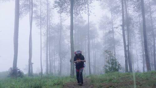 Full length of woman standing by trees in forest during winter