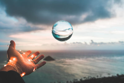 Person holding crystal ball against sky during sunset