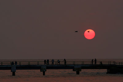 Silhouette people on beach against clear sky during sunset
