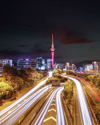 Light trails on road amidst buildings against sky at night