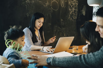 Father playing with children while mother using laptop at table in living room